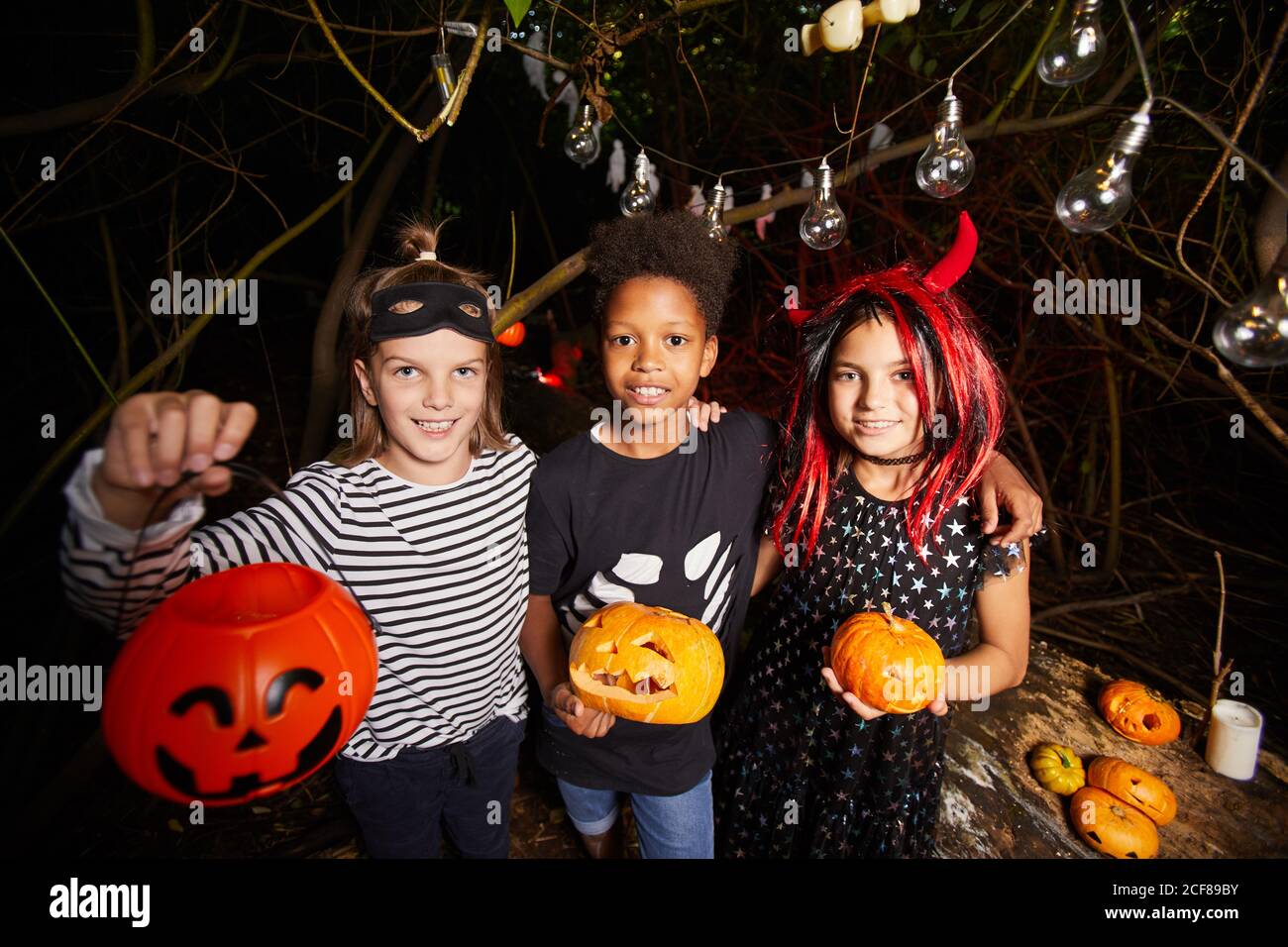 Portrait d'enfants heureux en costumes d'Halloween tenant des citrouilles et sourire à l'appareil photo dans l'obscurité Banque D'Images