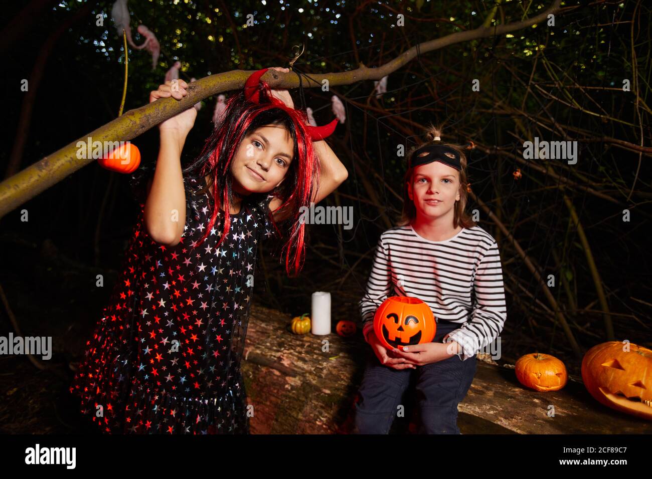 Portrait de deux filles regardant l'appareil photo tout en étant assis à l'extérieur Dans le noir pendant la fête d'Halloween Banque D'Images