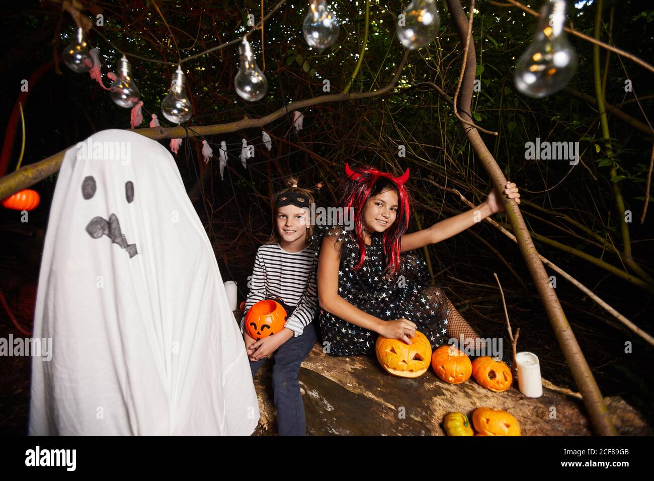Deux bonnes filles célèbrent Halloween avec leur ami costume fantôme ils sont assis parmi les citrouilles à l'extérieur Banque D'Images