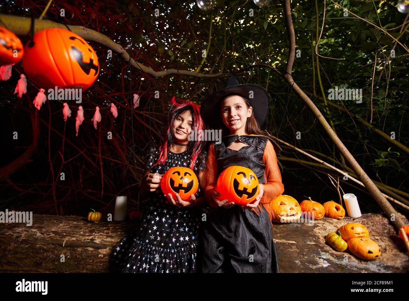 Portrait de deux filles en costumes tenant des citrouilles en peluche et souriant à la caméra, ils sont à la fête dans le sombre Banque D'Images