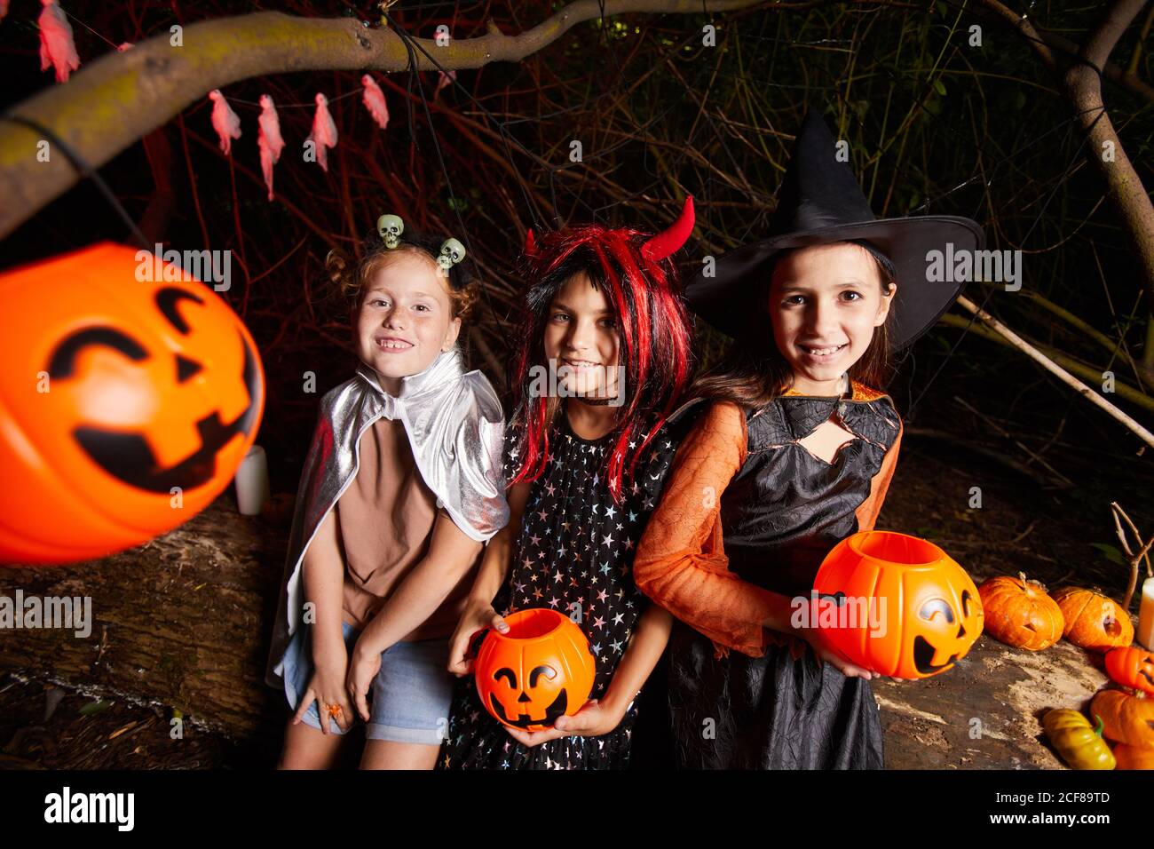 Portrait d'amis en costumes d'Halloween souriant à l'appareil photo pendant assis dans le noir parmi les citrouilles de la partie Banque D'Images