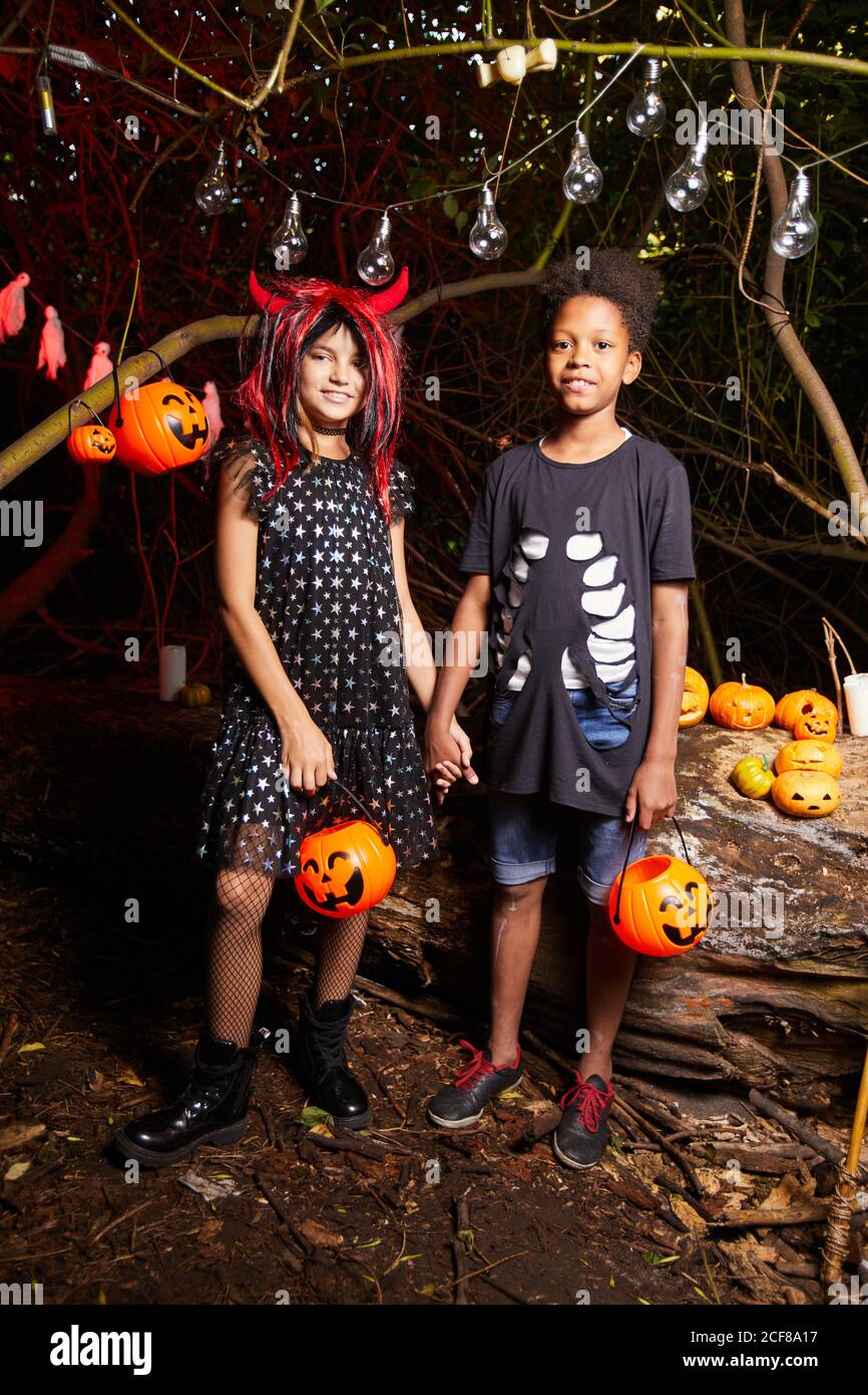 Portrait de deux amis en costumes debout et tenant les mains À la fête d'Halloween dans le noir Banque D'Images