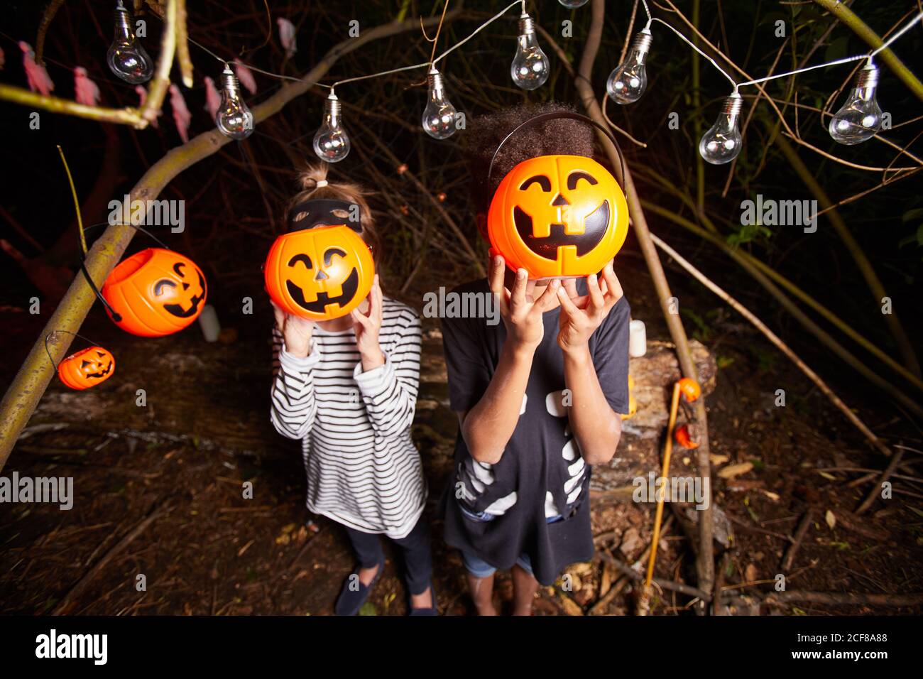 Portrait de deux enfants tenant des citrouilles en peluche devant Leurs visages tout en se tenant dans l'obscurité dehors à Halloween fête Banque D'Images