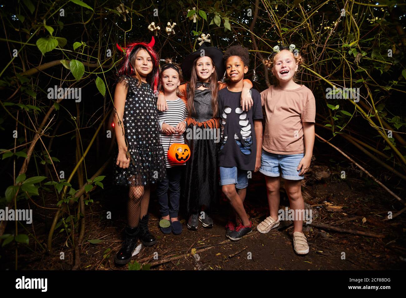 Portrait des enfants heureux en costumes d'Halloween debout dans le forêt sombre et souriant à l'appareil photo Banque D'Images