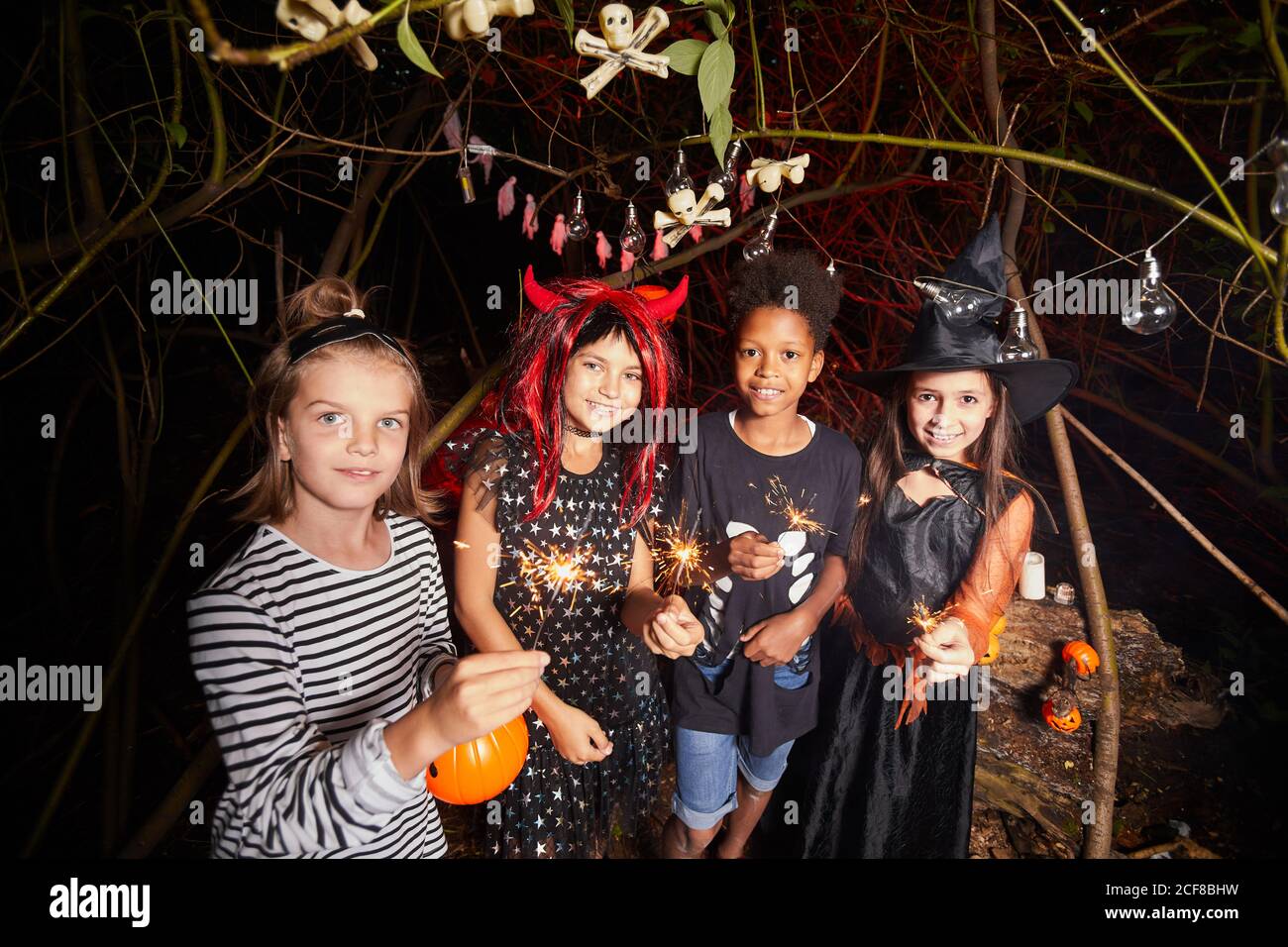 Portrait des enfants en costumes tenant des spamisseurs et souriant à Appareil photo pendant la fête d'Halloween dans la forêt Banque D'Images