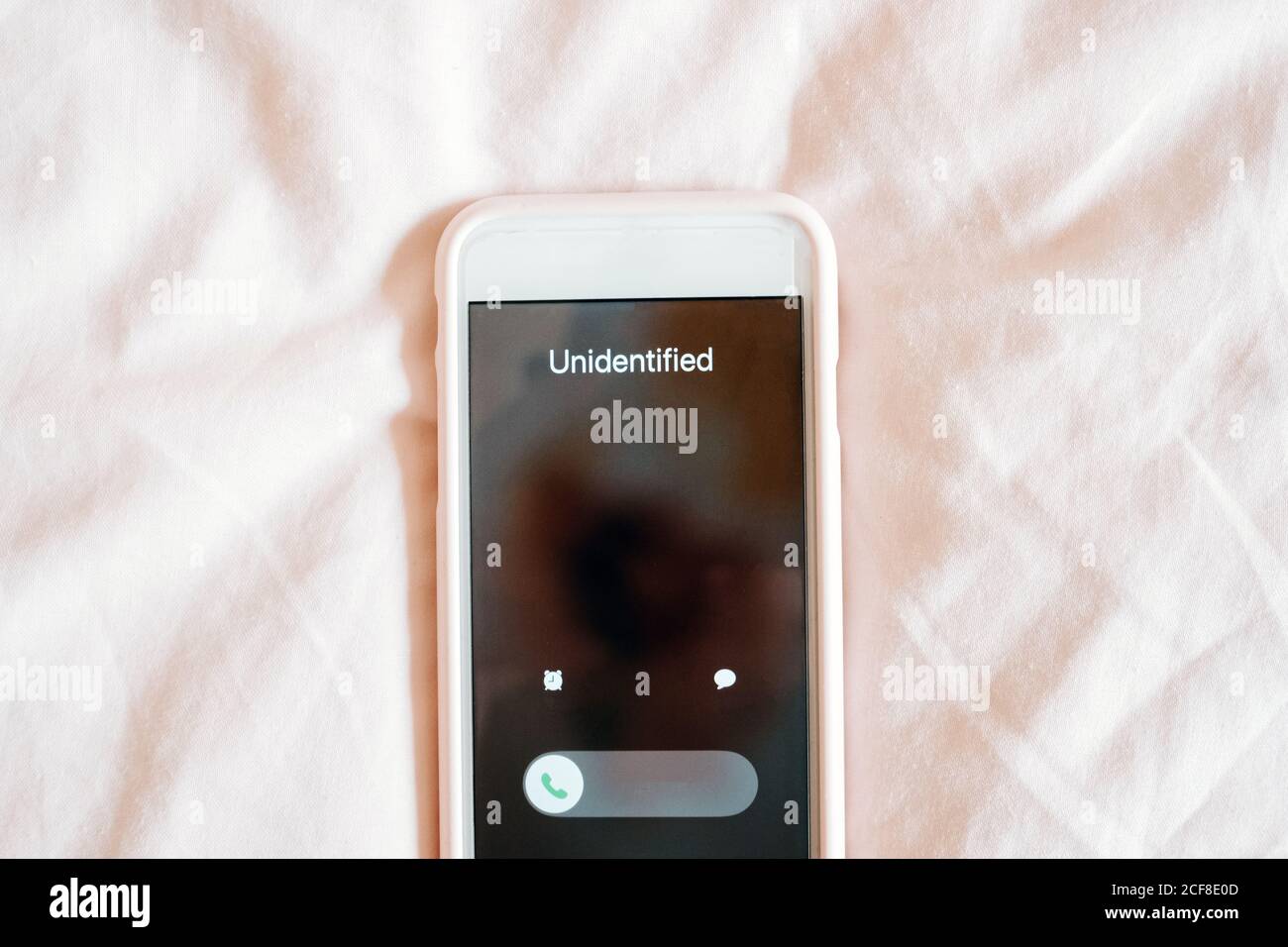 Écran du téléphone avec appel entrant d'un abonné méconnaissable contre le lit Banque D'Images