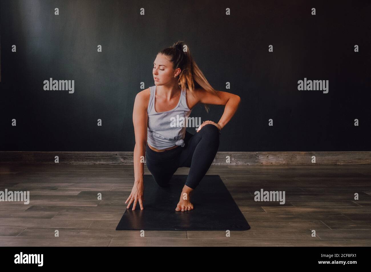 Grand angle de la femme confiante barefooted dans les vêtements de sport stretching body dans eka pada rajakapotasana deux positions sur le tapis et regarder loin tout en s'entraîner dans la salle d'entraînement moderne et spacieuse Banque D'Images