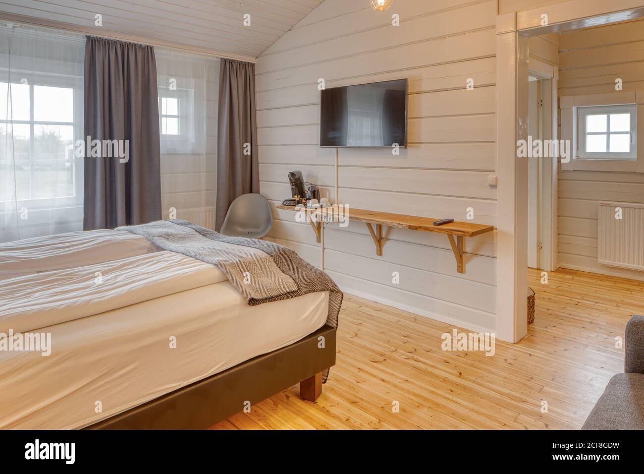 Chambre confortable avec murs en bois blanc et grand lit moelleux avec canapé gris confortable près de l'éclairage au sol Banque D'Images