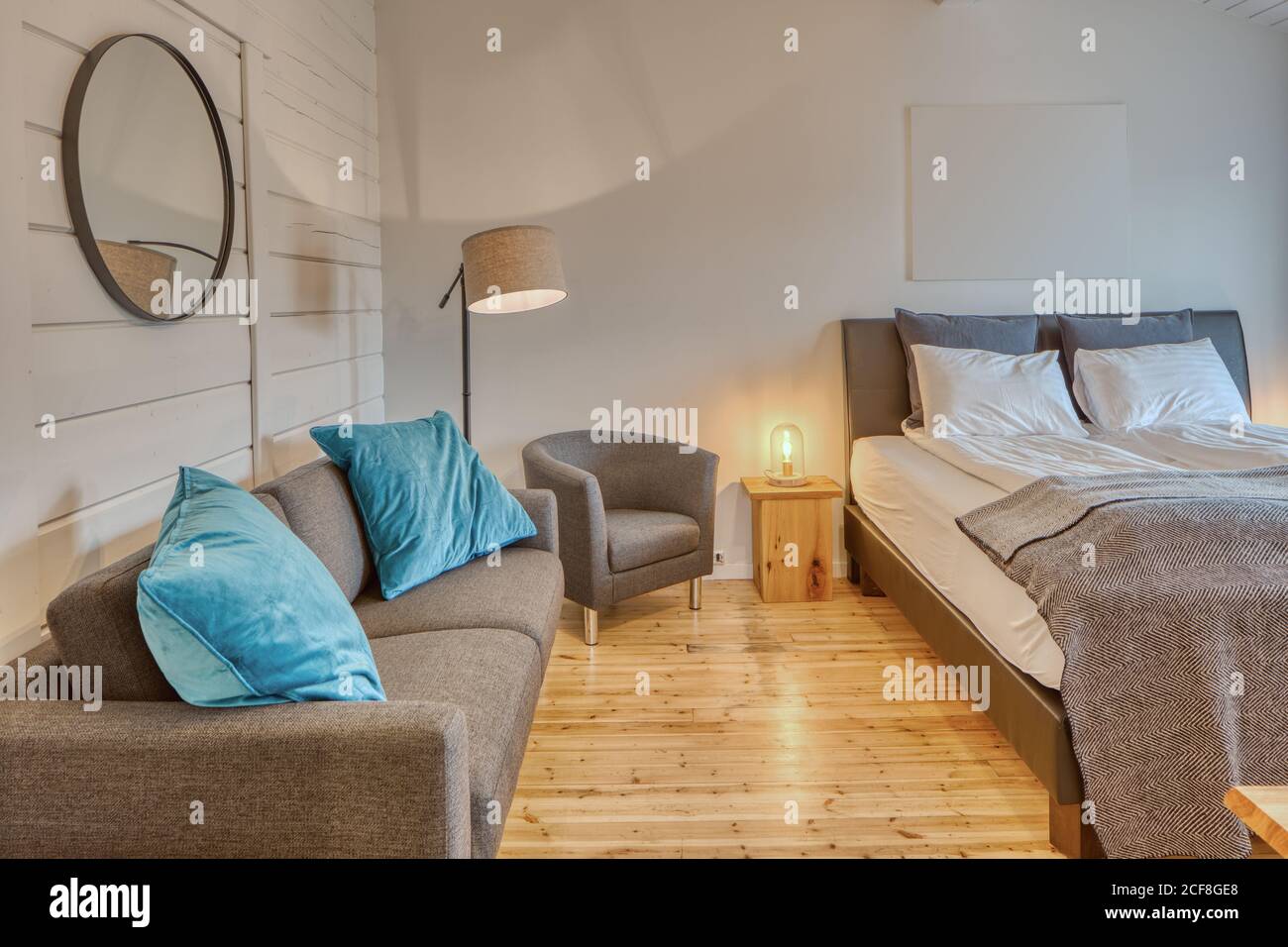 Chambre confortable avec murs en bois blanc et grand lit moelleux avec canapé gris confortable près de l'éclairage au sol Banque D'Images