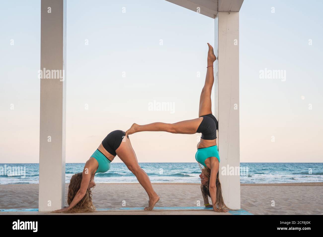 Les femmes sportives qui font acroyoga posture double chien sur le sable plage Banque D'Images