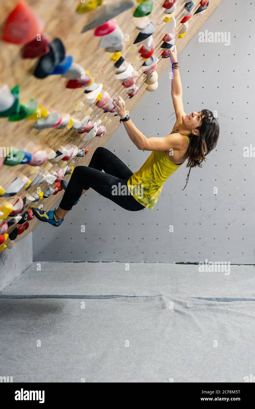 Vue latérale depuis le dessous de la femme concentrée dans les vêtements de  sport suspendus sur un mur raide au-dessus des tapis dans le centre moderne  d'escalade Photo Stock - Alamy