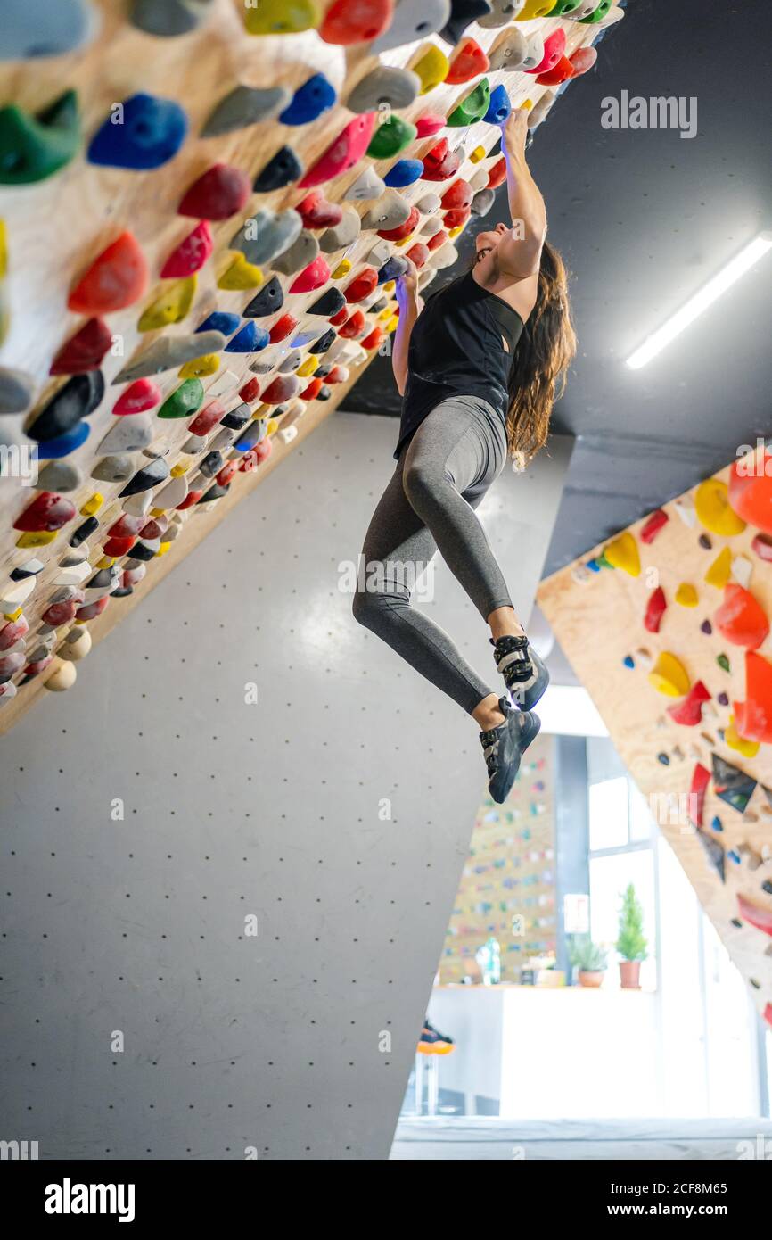 Vue latérale depuis le dessous de la femme concentrée dans les vêtements de  sport suspendus sur un mur raide au-dessus des tapis dans le centre moderne  d'escalade Photo Stock - Alamy