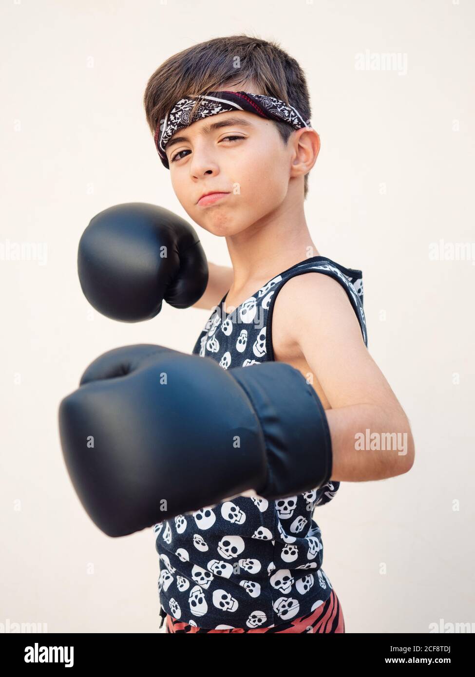 Petit garçon concentré dans des gants de boxe noirs battant punch à appareil photo Banque D'Images