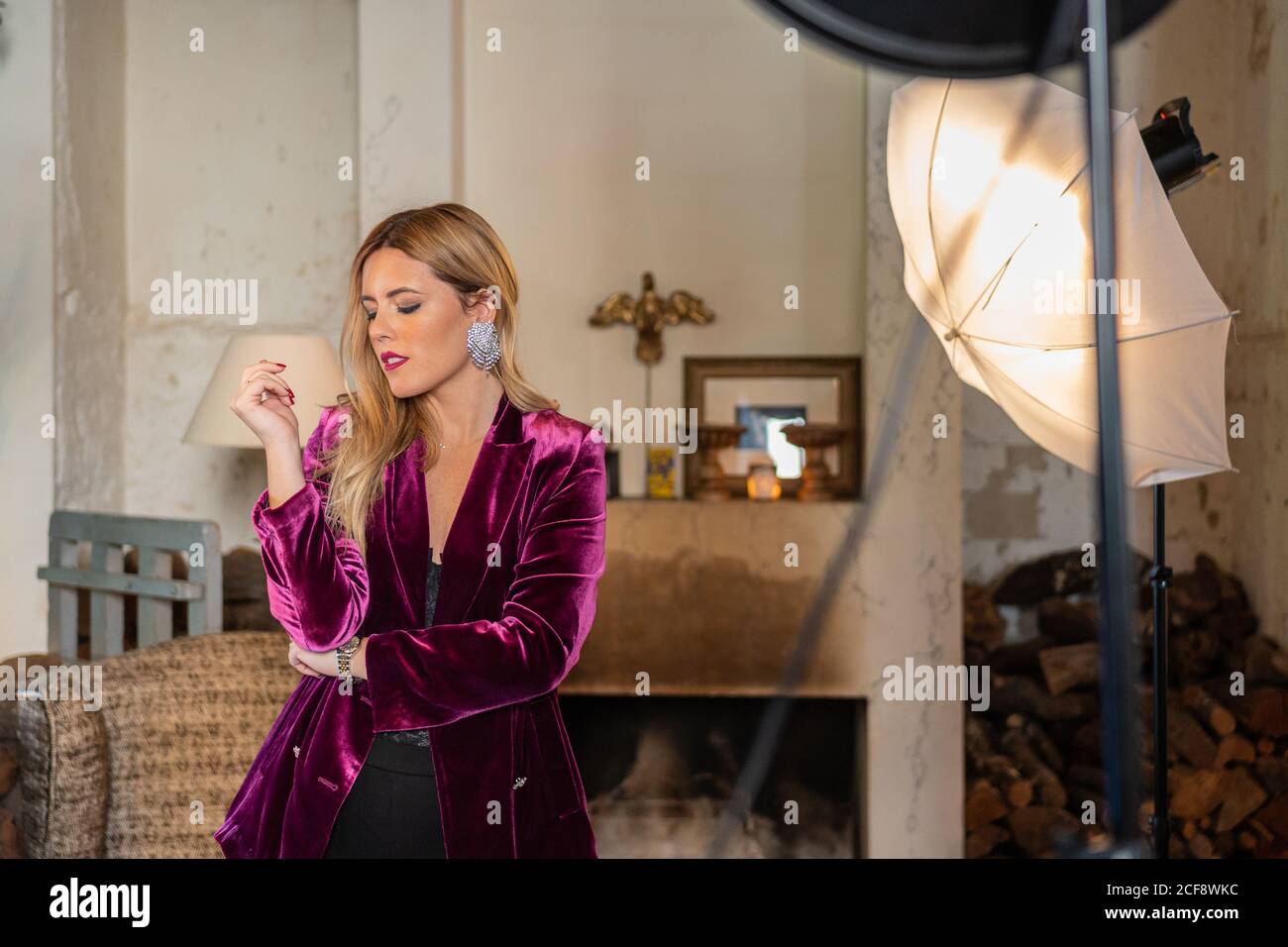 Homme méconnaissable se focalisant et prenant des photos avec un appareil photo de séduisant femme adulte dans des vêtements colorés élégants assis dans un fauteuil contre intérieur rustique vintage dans la lumière vive de la boîte souple et réflecteur en studio photo Banque D'Images