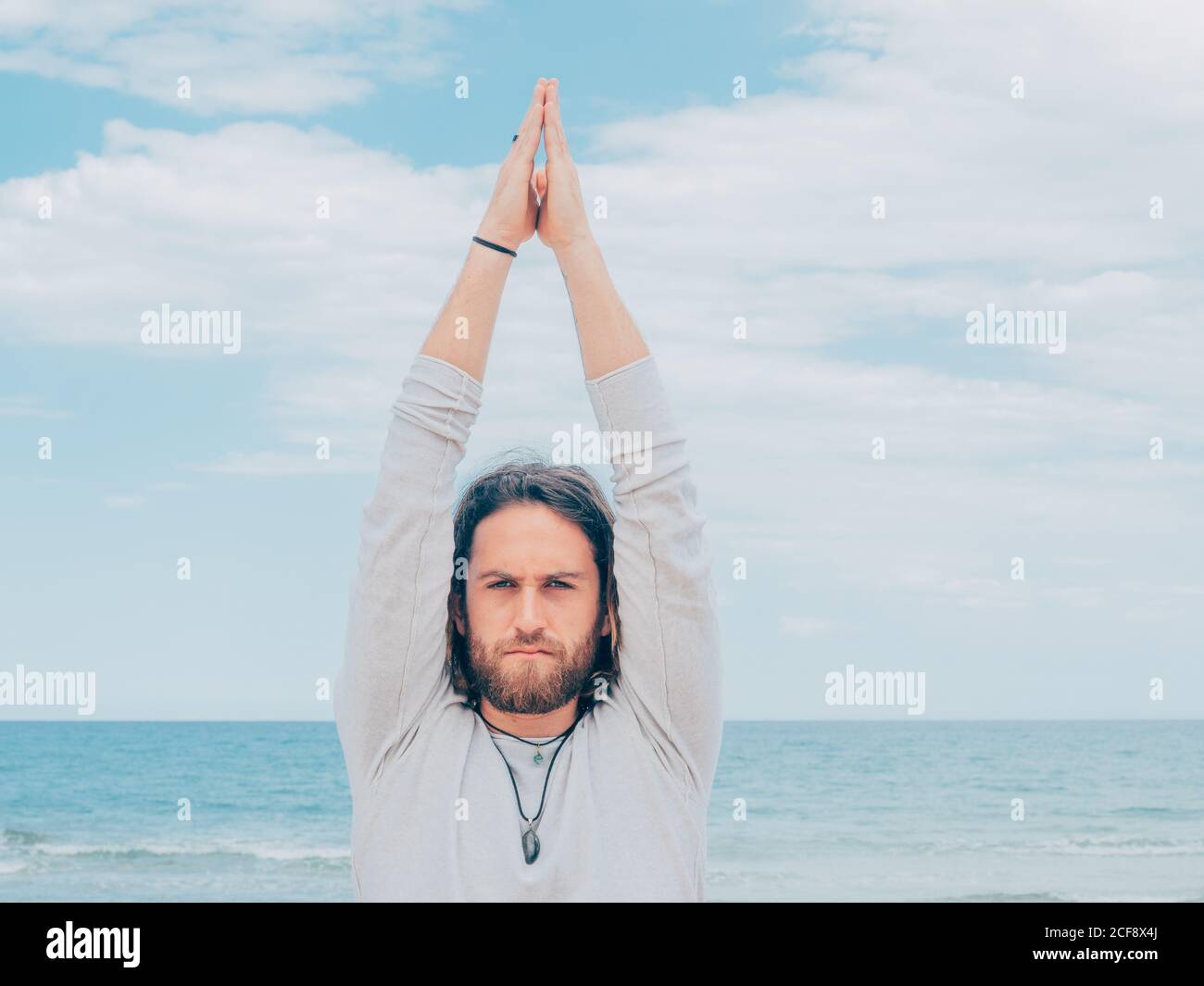 Entraînement sportif masculin barbu sur la mer tranquille et faisant du yoga asana contre la mer bleue et le ciel Banque D'Images