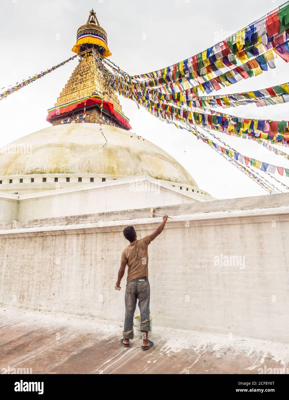 NÉPAL, BOUDHANATH STUPA - 19 AOÛT 2014 : vue arrière du jeune ouvrier peignant le mur de pierre avec le lavage à la chaux Banque D'Images