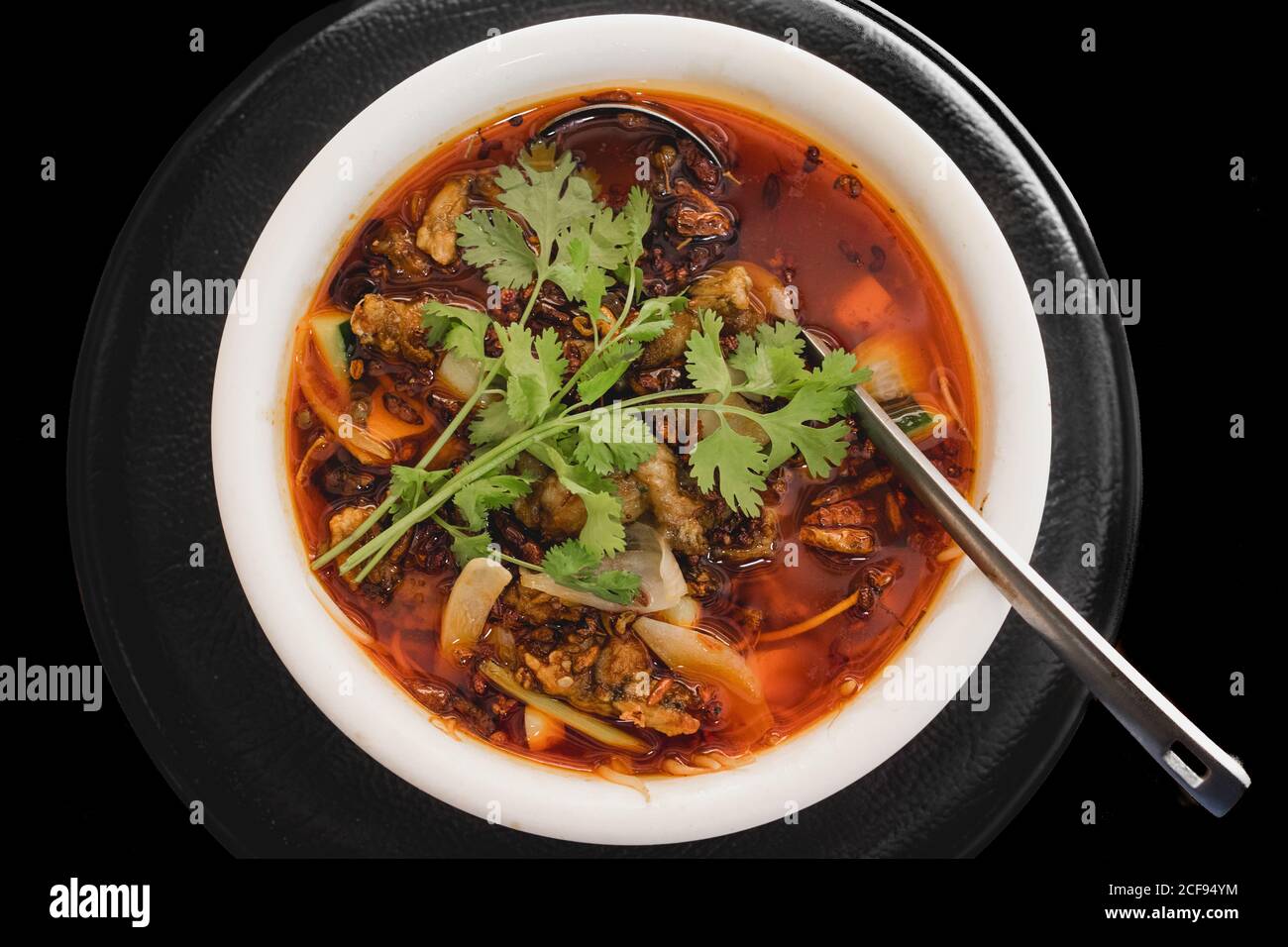 De dessus une délicieuse soupe de grenouille chaude avec de la viande de grenouille, de l'oignon, du concombre et de la coriandre sur une assiette sur fond noir Banque D'Images