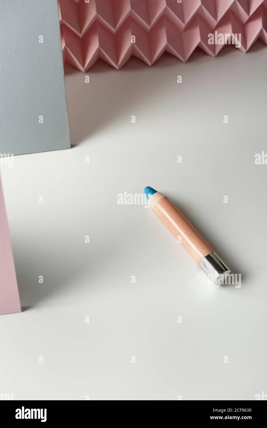 Crayons cosmétiques:, crayon de maquillage bleu, fond moderne avec des reliefs de chevron rose. Concept de maquillage Banque D'Images