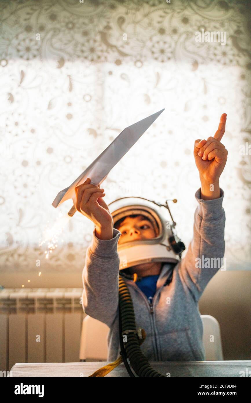 Un garçon fantastique dans un casque d'astronaute jouant avec un avion en papier à accueil Banque D'Images