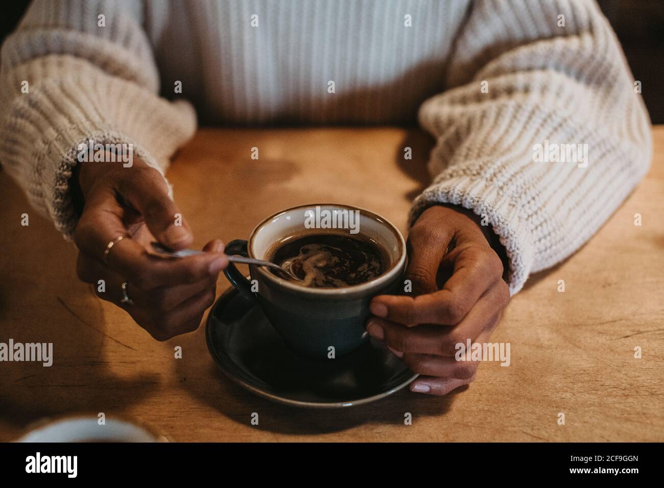 De dessus, crop mains de femelle méconnaissable assis au bois table contenant du café chaud dans une tasse rustique Banque D'Images