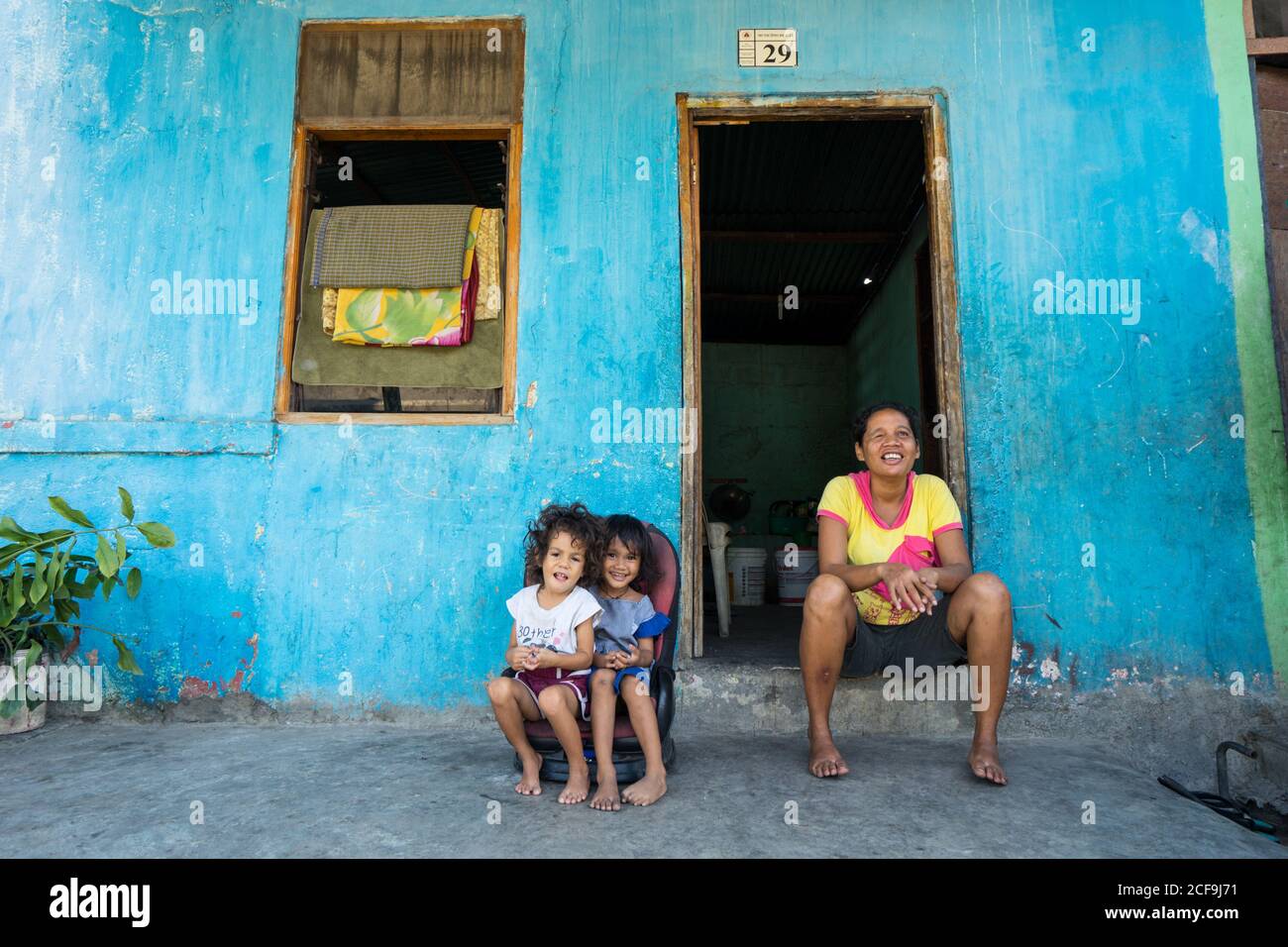 Dili, Timor oriental - 09 AOÛT 2018: Femme gaie et petites filles regardant la caméra tout en étant assis à la porte de la maison pauvre Banque D'Images