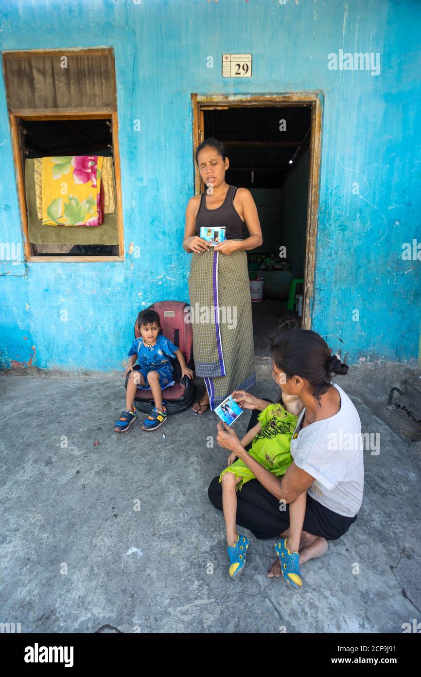 Dili, Timor oriental - 09 AOÛT 2018 : jeunes femmes asiatiques avec de petits enfants regardant des photos professionnelles dans la cour de la maison pauvre Banque D'Images