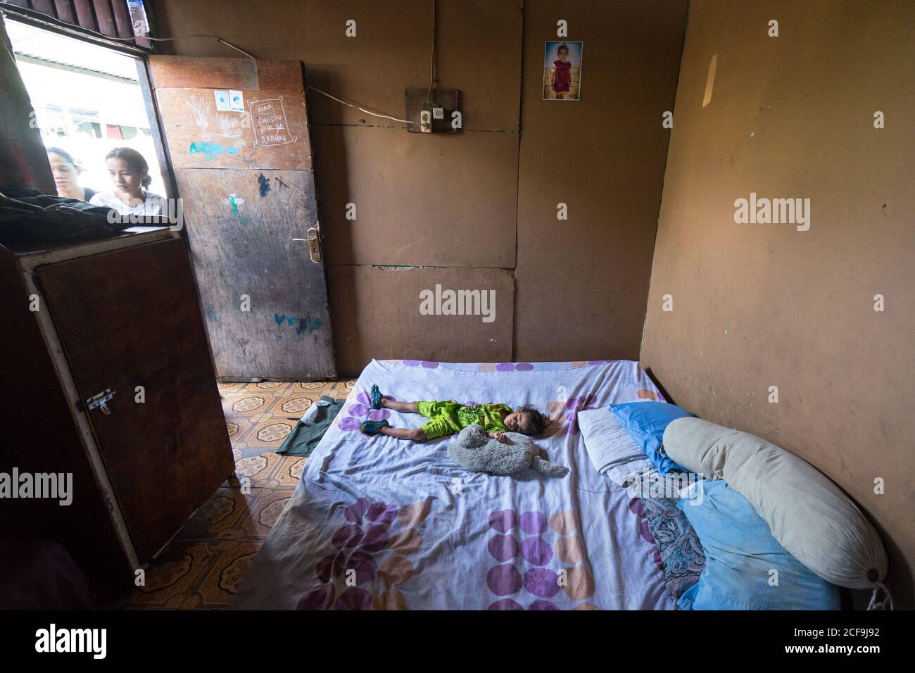 Dili, Timor oriental - 09 AOÛT 2018: Petit enfant dormant sur un grand lit dans une maison pauvre et misérable avec des murs vides et peu de meubles Banque D'Images