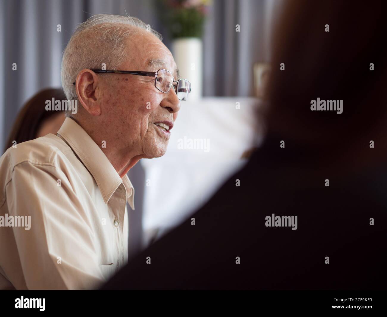 Un très vieux homme asiatique parlant heureusement pendant qu'il est entouré sa famille Banque D'Images
