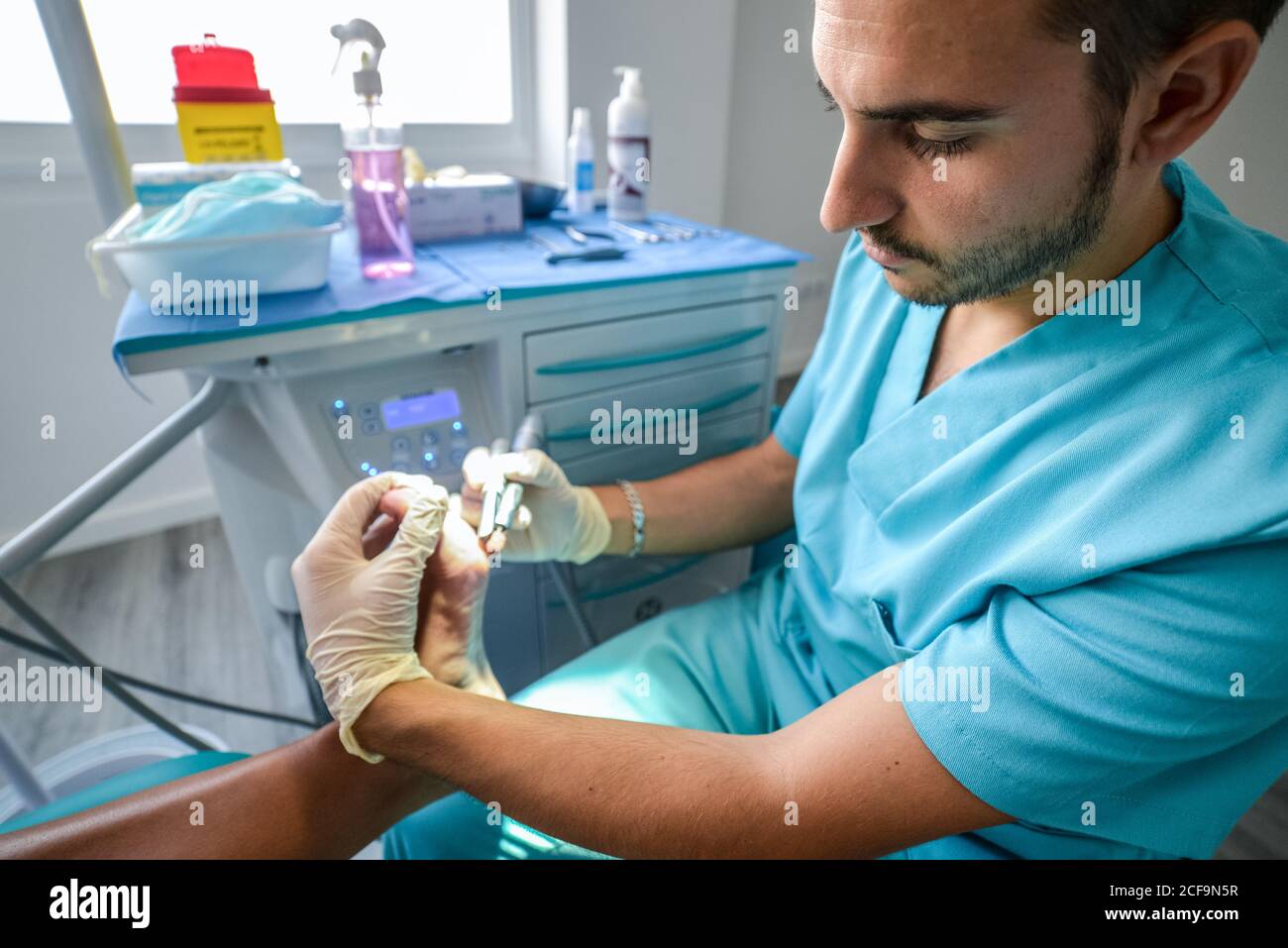 Vue latérale d'un médecin spécialiste qualifié en uniforme bleu et gants de protection utilisant un équipement professionnel lors de l'exécution de la procédure avec le pied du patient Banque D'Images