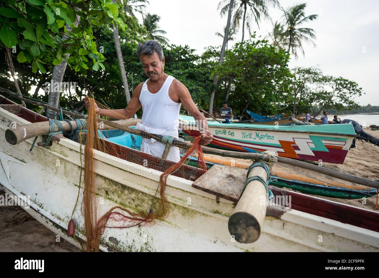 Tangalle, Sri Lanka - 28 juillet 2019 : ancien pêcheur ethnique en vêtement blanc léger préparant le filet de pêche à bord d'un bateau Banque D'Images