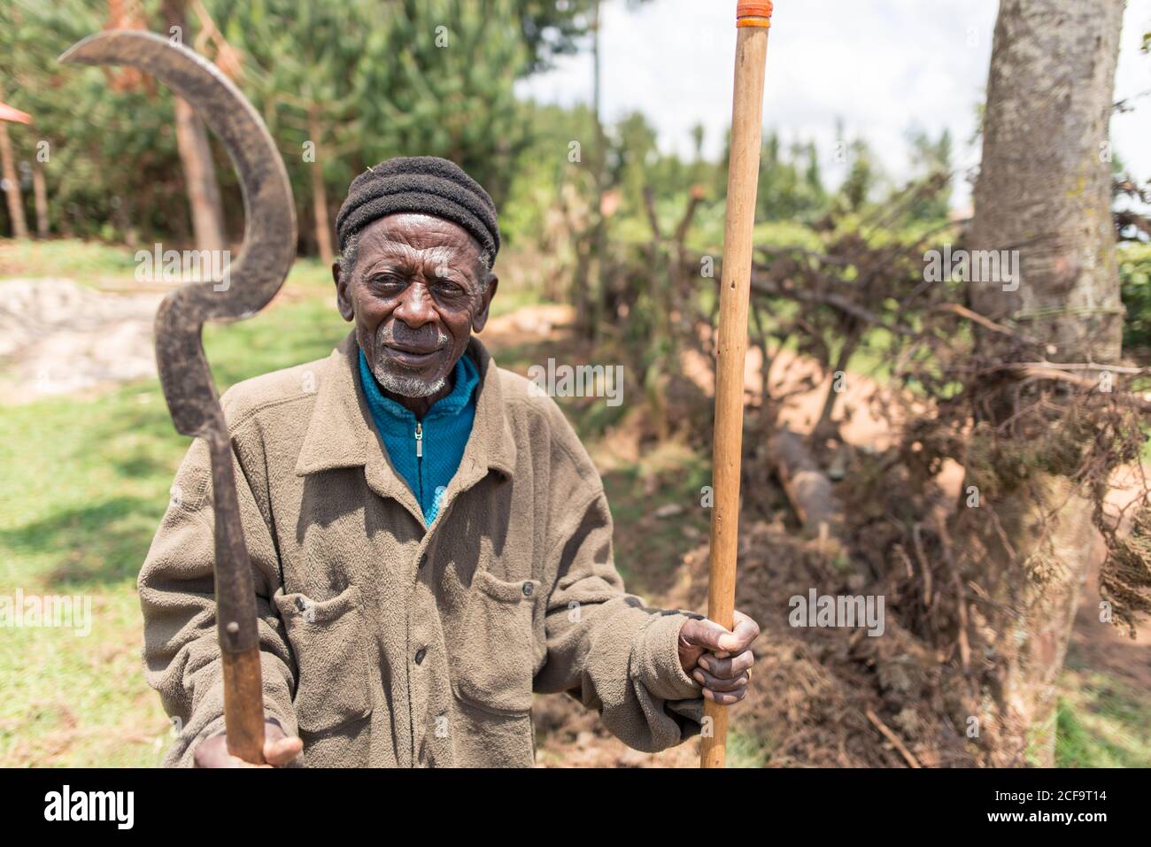 Ouganda - novembre 26 2016 : vieil homme africain avec hache et bâton regardant la caméra au milieu d'une forêt dans la campagne Banque D'Images