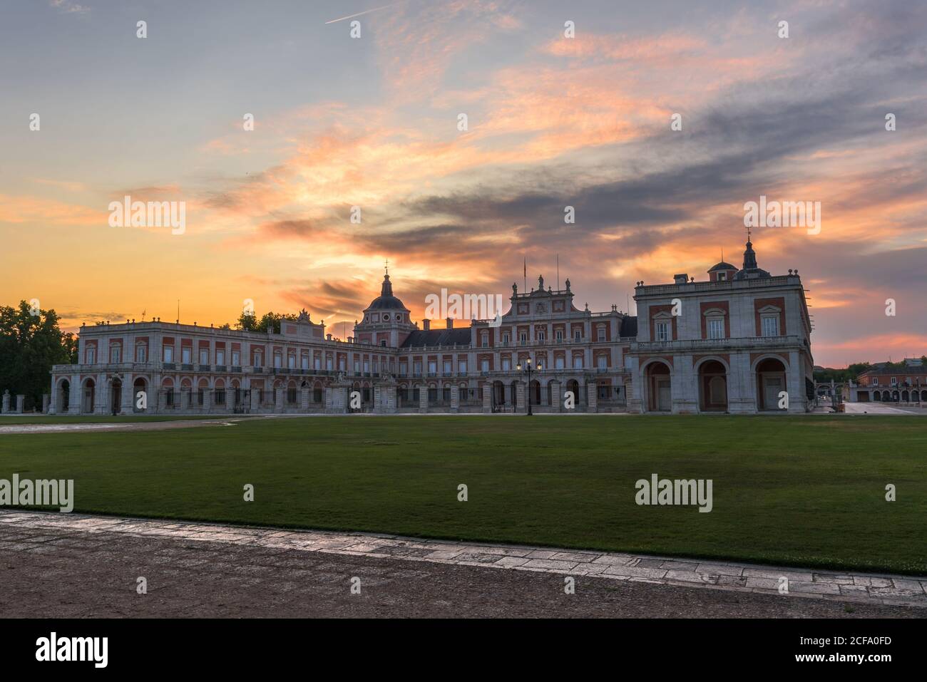 Façade de palais médiéval avec allée et pelouses vertes sous ciel de coucher de soleil Banque D'Images