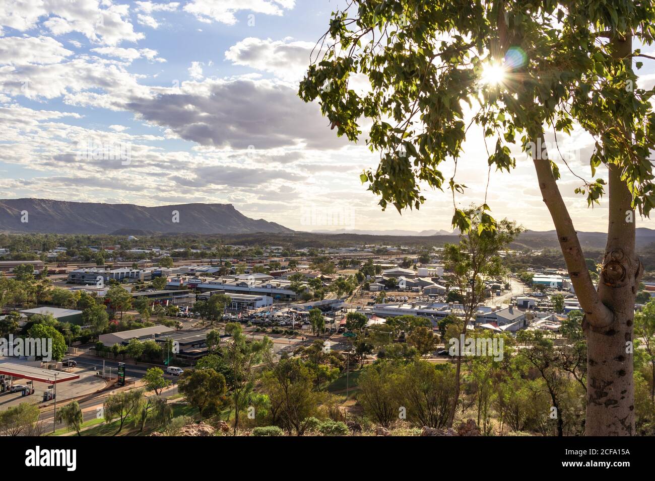 Vue sur la ville d'Alice Springs depuis la colline d'Anzac. Montagnes MacDonnell chaîne en arrière-plan. Soleil brillant parmi les feuilles de l'arbre à l'heure du coucher du soleil. Nuageux s Banque D'Images