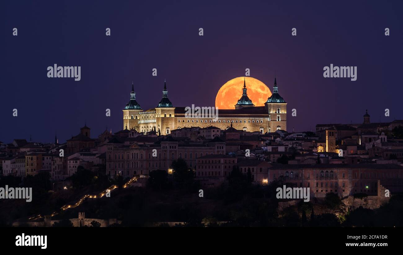 Magnifique paysage d'un ancien palais illuminé construit au-dessus de la ville Nuit colorée avec pleine lune rouge à Tolède Banque D'Images