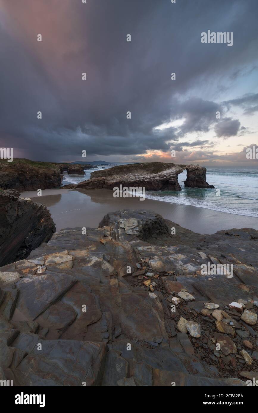 Rochers rugueux sur le rivage d'un océan calme sous des nuages gris dans un ciel lumineux Banque D'Images