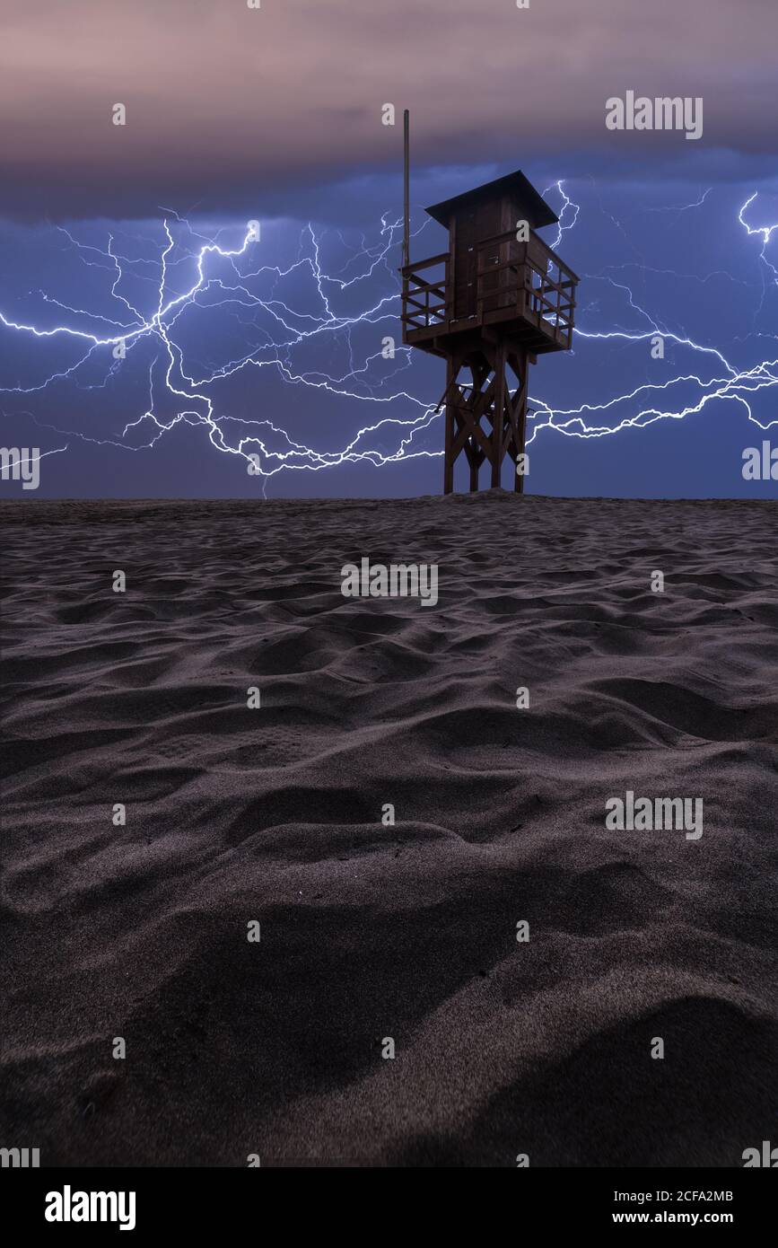 Angle bas de la tour solitaire située sur un terrain sablonneux désertique contre un ciel sombre et sombre illuminé par des éclairs lumineux pendant la nuit heure Banque D'Images