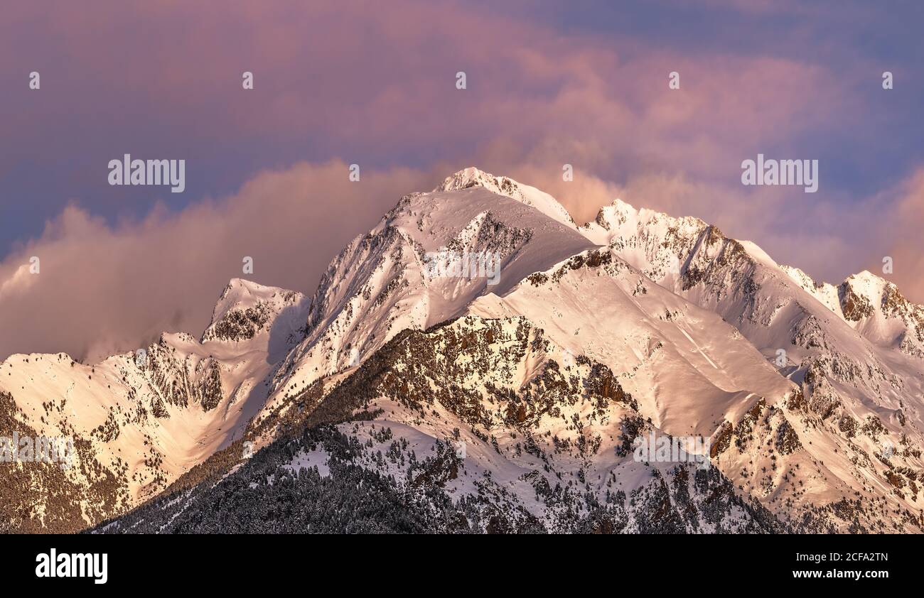 Pics de montagne pointus partiellement couverts de neige et entourés de brouillard sous un ciel pittoresque et nuageux rose et violet à la tombée de la nuit en hiver Banque D'Images