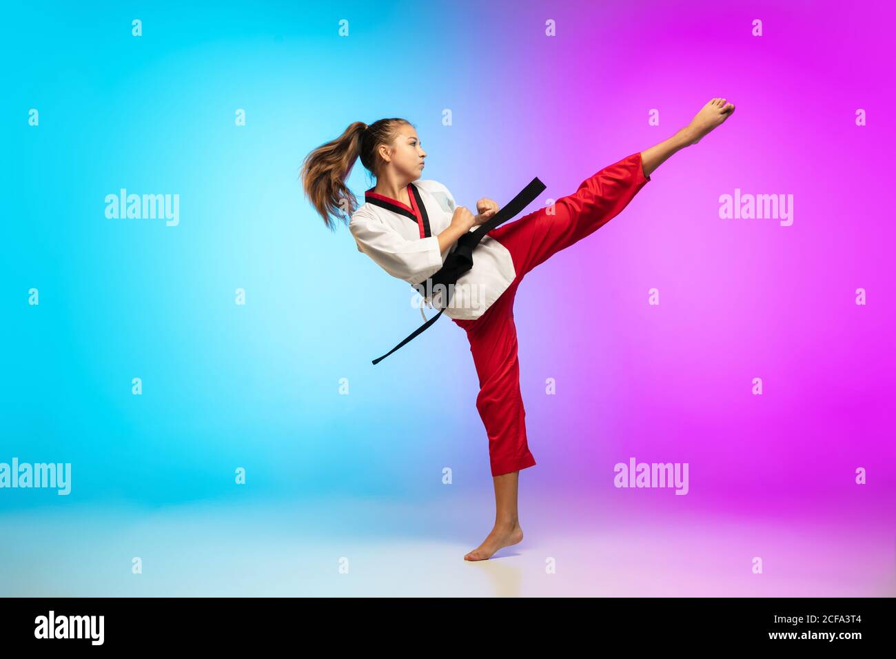 Frapper. Karate, taekwondo fille avec ceinture noire isolée sur fond dégradé  dans la lumière de néon. Petit modèle caucasien, entraînement sportif pour  enfants en mouvement et en action. Sport, mouvement, concept d'enfance