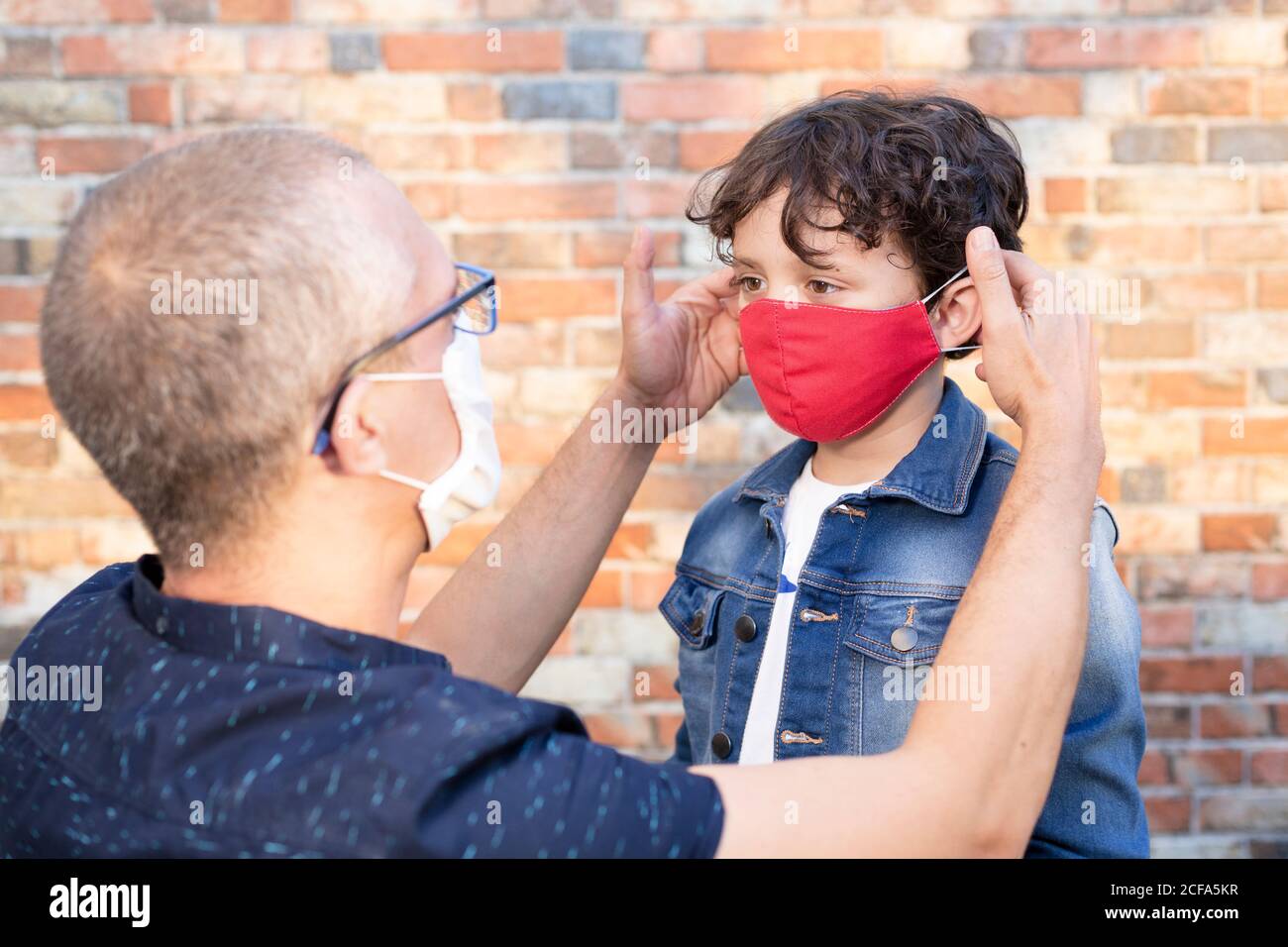 Homme portant un masque de protection mettant un masque facial sur un son fils dans la rue. Concept de sécurité pendant l'éclosion de Covid-19. Banque D'Images