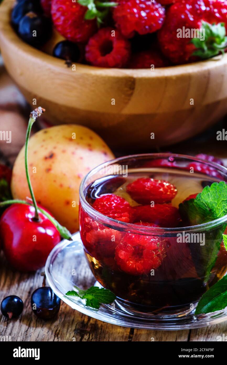 Thé aux fruits d'été avec menthe dans une tasse de verre, fruits frais et baies, fond en bois foncé, foyer sélectif Banque D'Images