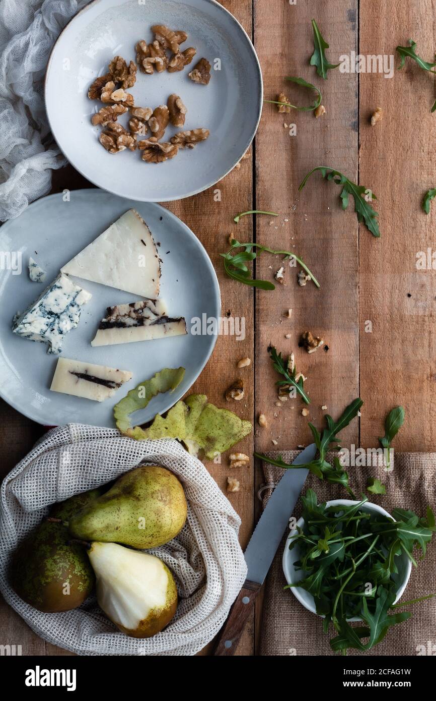 Vue de dessus des assiettes avec des noix et du fromage à proximité sac de coton avec poires mûres et bol avec arugula fraîche sur la table de bois pendant la préparation de la salade Banque D'Images