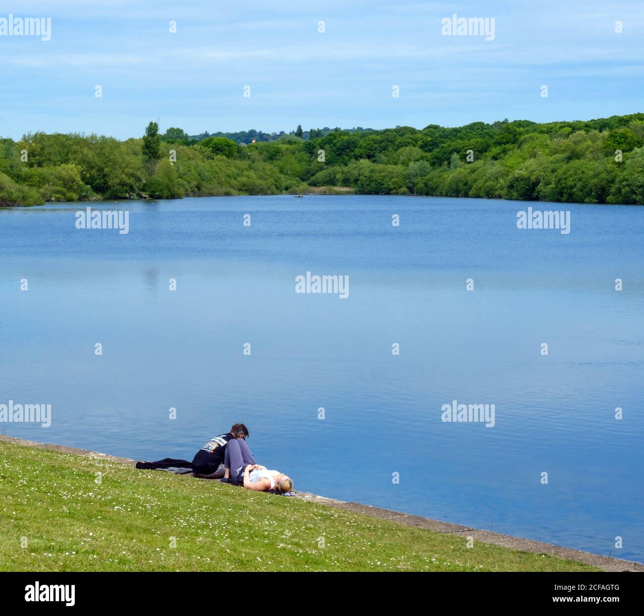 Un jeune couple s'assoit sur l'herbe à côté de l'eau au réservoir du Lido de Ruislip, à Hillingdon, dans le nord-ouest de Londres Banque D'Images