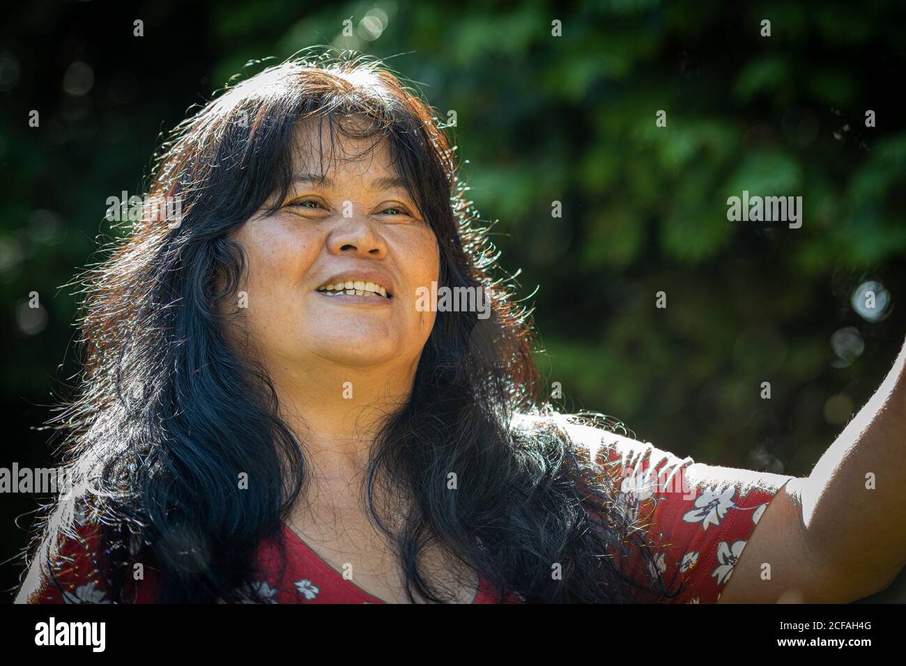 Gros plan d'une femme d'âge moyen, dans ses années 50, asiatique avec des bulles de savon. Feuilles vertes en arrière-plan Banque D'Images