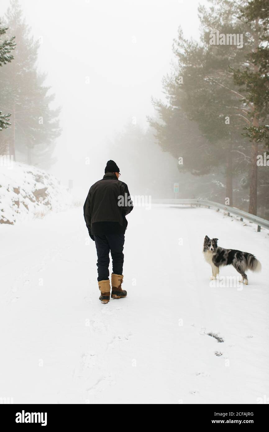 un homme et son chien méconnaissables marchent par une journée brumeuse avec de la neige Banque D'Images