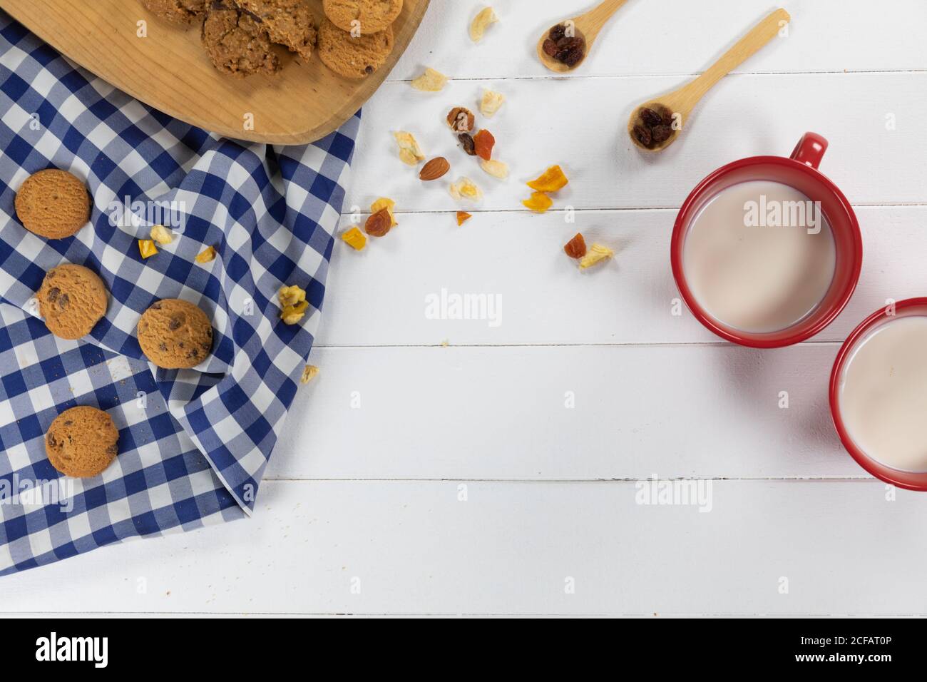 Vue sur les biscuits, cuillères avec fruits secs et noix et deux tasses avec lait sur bois Banque D'Images