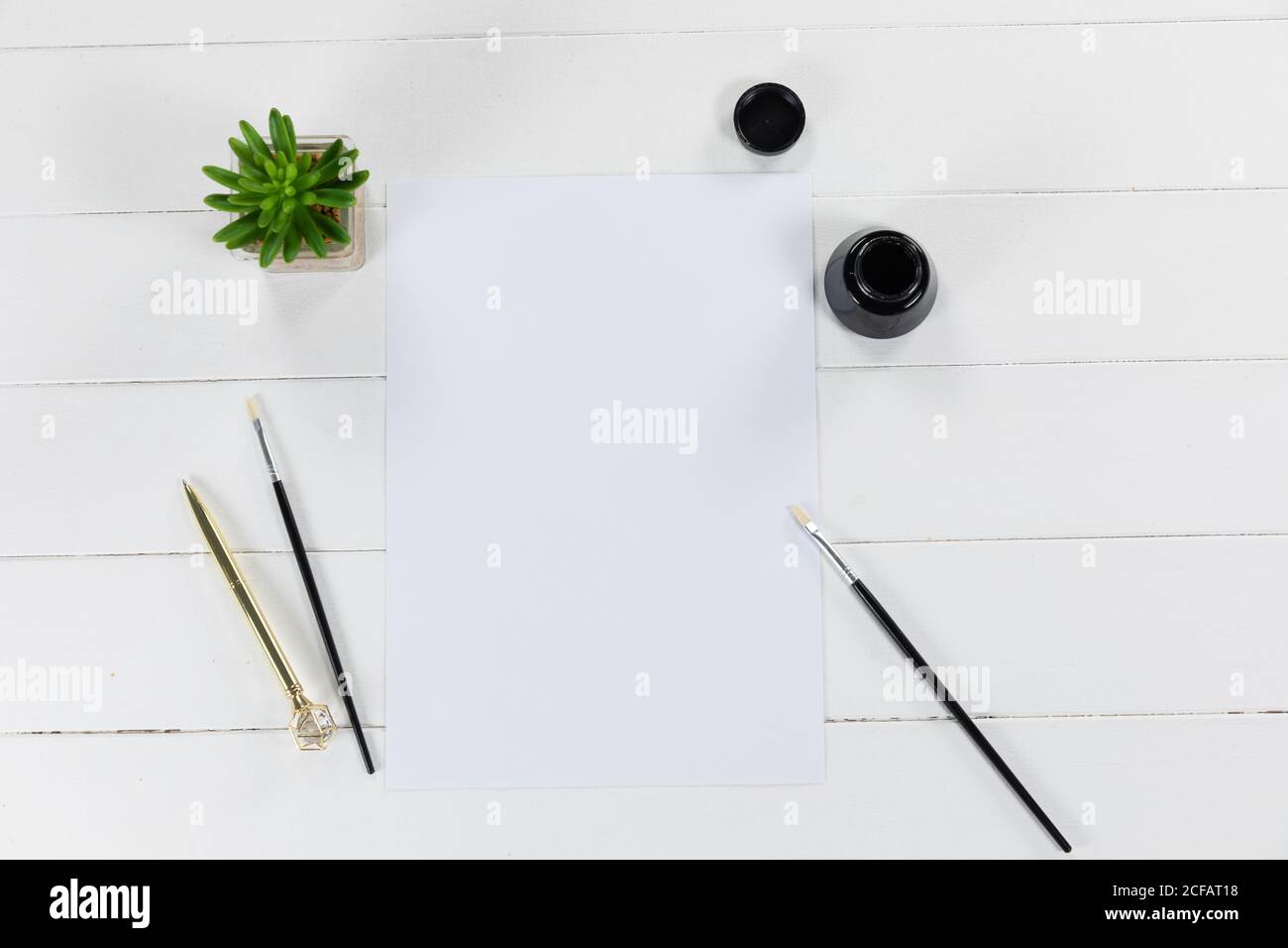 Vue d'une feuille de papier blanc, d'une bouteille d'encre noire et de pinceaux avec une plante verte sur blanc ordinaire Banque D'Images