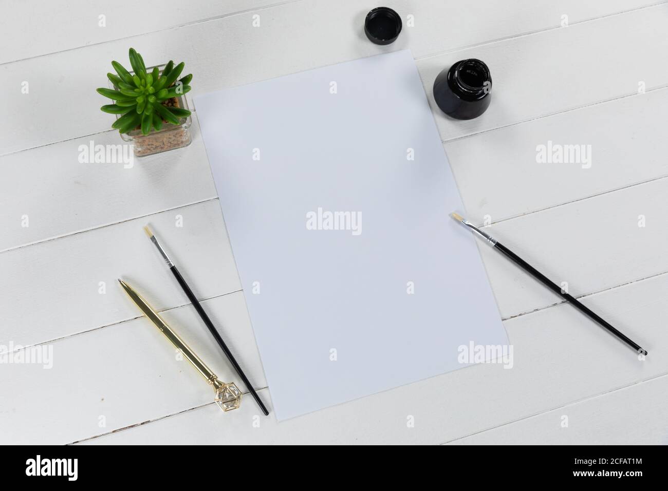 Vue d'une feuille de papier blanc, d'une bouteille d'encre noire et de pinceaux avec une plante verte sur blanc ordinaire Banque D'Images