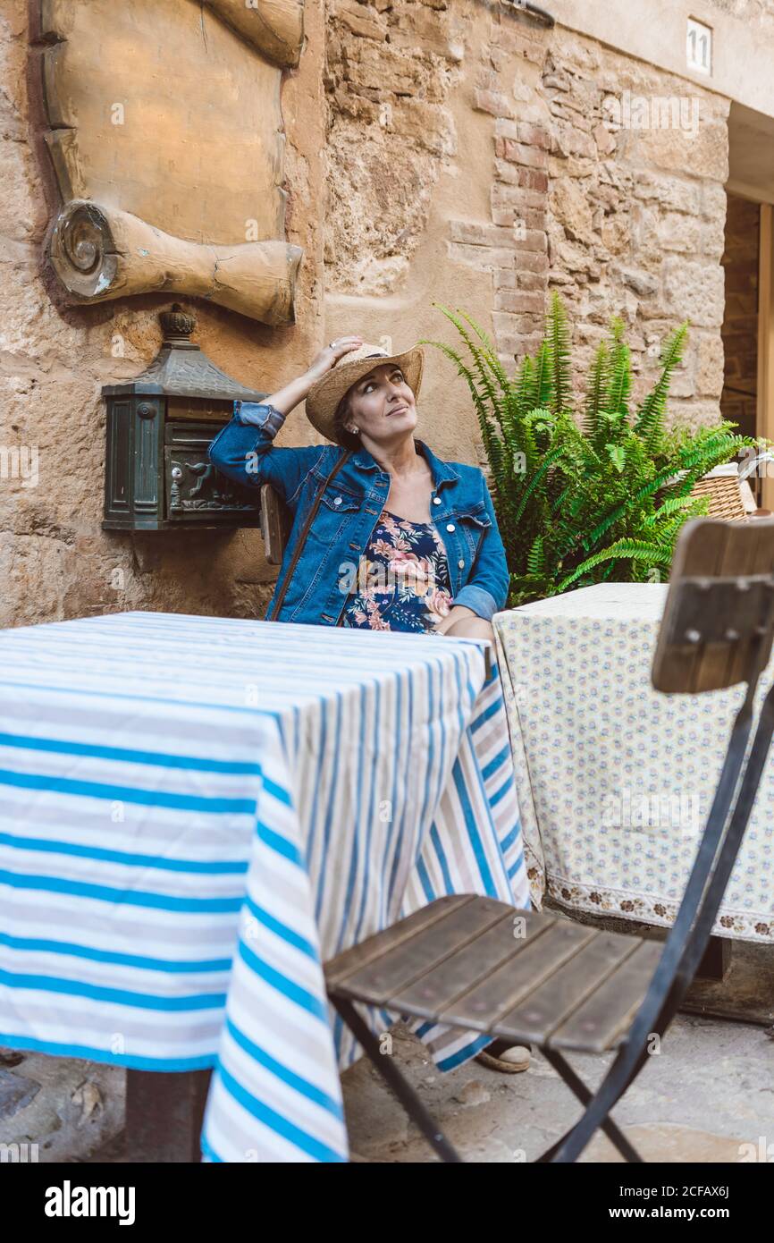 Femme avec chapeau et robe assis sur la terrasse d'un restaurant Banque D'Images