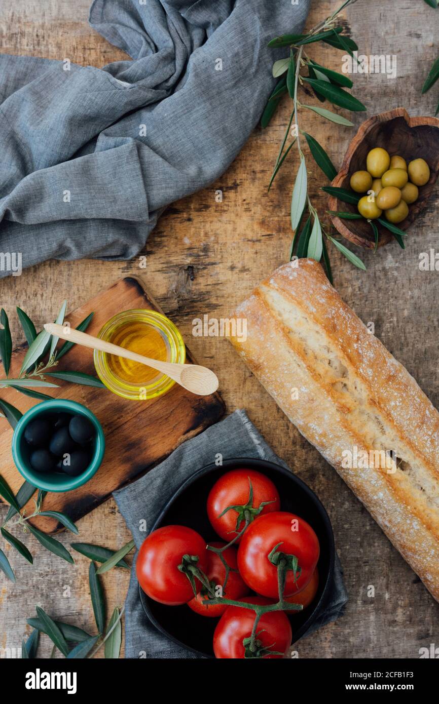 Vue de dessus composition de pain frais maison mis sur table en bois près des tomates rouges mûres avec du vert et du noir olives et huile d'olive Banque D'Images