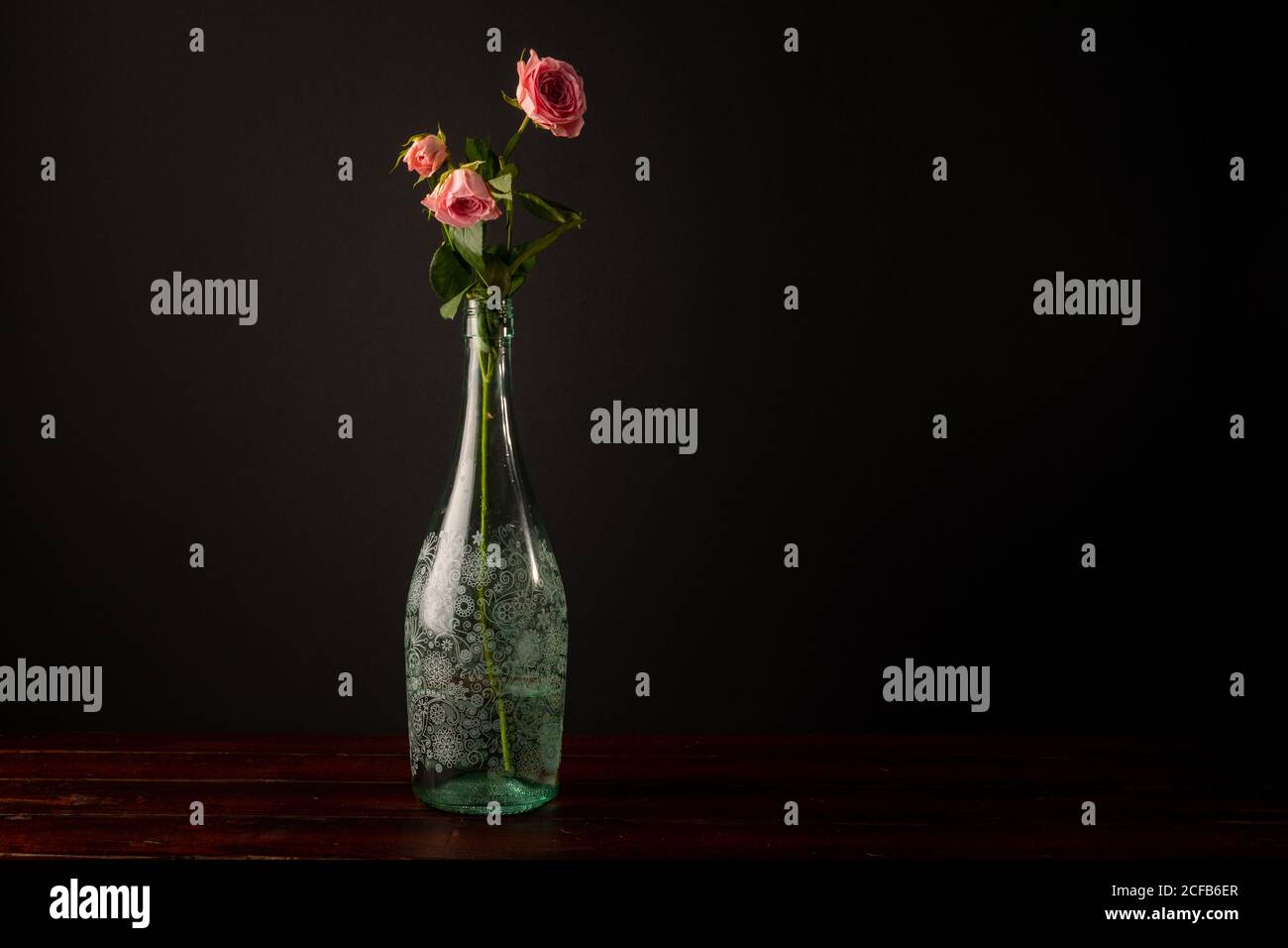 Jolies fleurs roses placées dans un élégant vase en verre sur bois plan d'examen sur fond gris foncé Banque D'Images